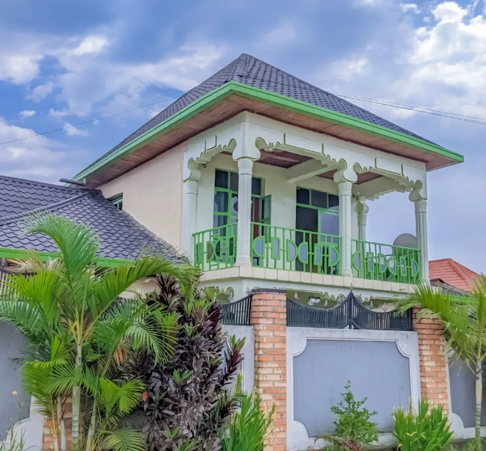 The house from the street, with its green gate and palms