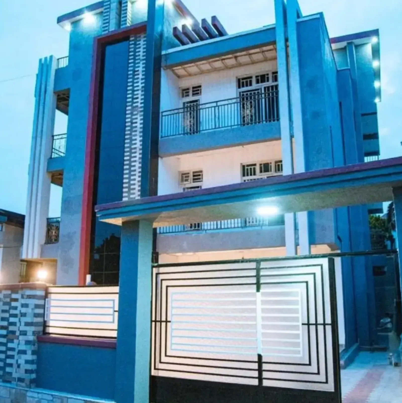 A tall modern blue house lit at dusk, with balconies and a gate